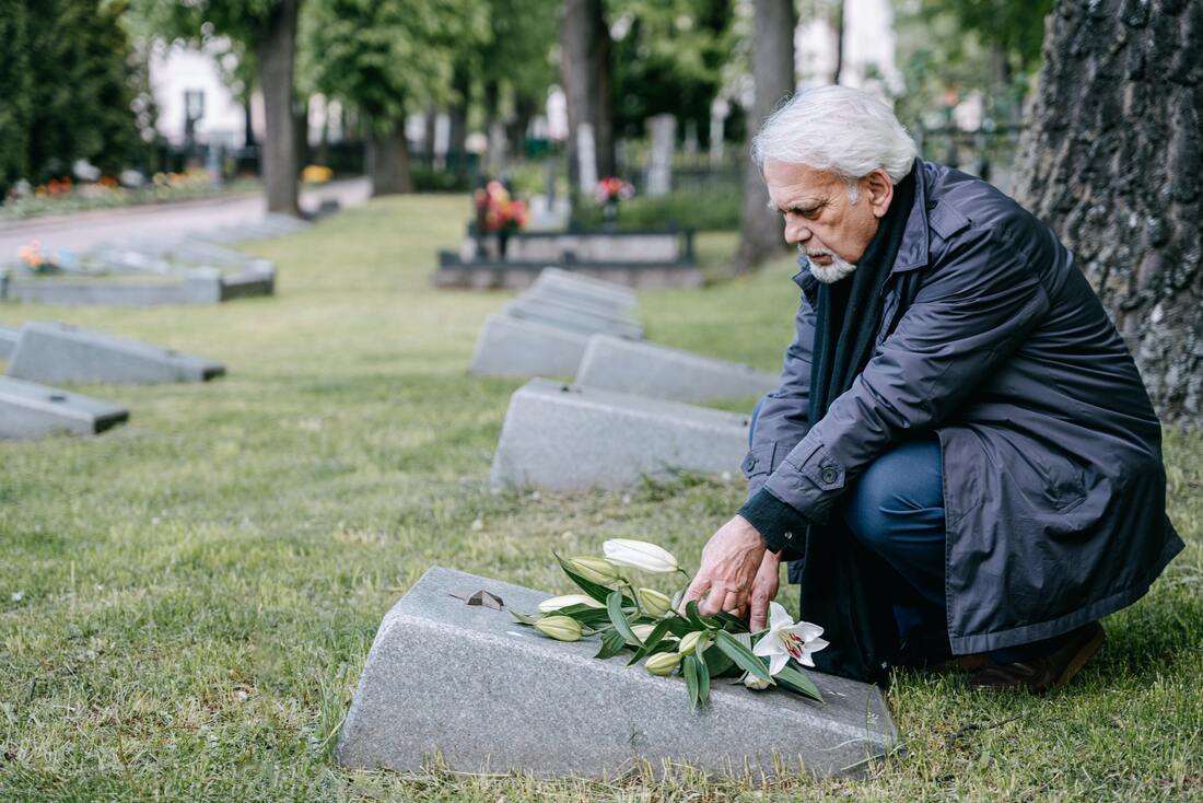 An elderly man places flowers on a grave.
