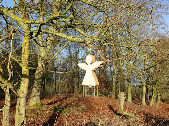 A small wooden angel hanging from a tree in woodland.